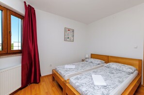 Egy hálószoba két ágyjal, vörös függönnyel ellátott ablakkal, radiátorral és a falra akasztott képpel.