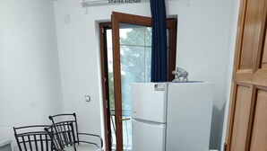 A shared kitchen with a white refrigerator, a dining table with chairs, and a view of the outdoors through a window. - Rooms Nada (Seline)