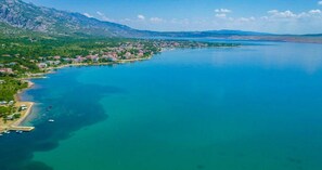 An aerial view of a coastal town with a clear blue sea, a marina with boats, and a mountainous backdrop. - Rooms Nada (Seline)