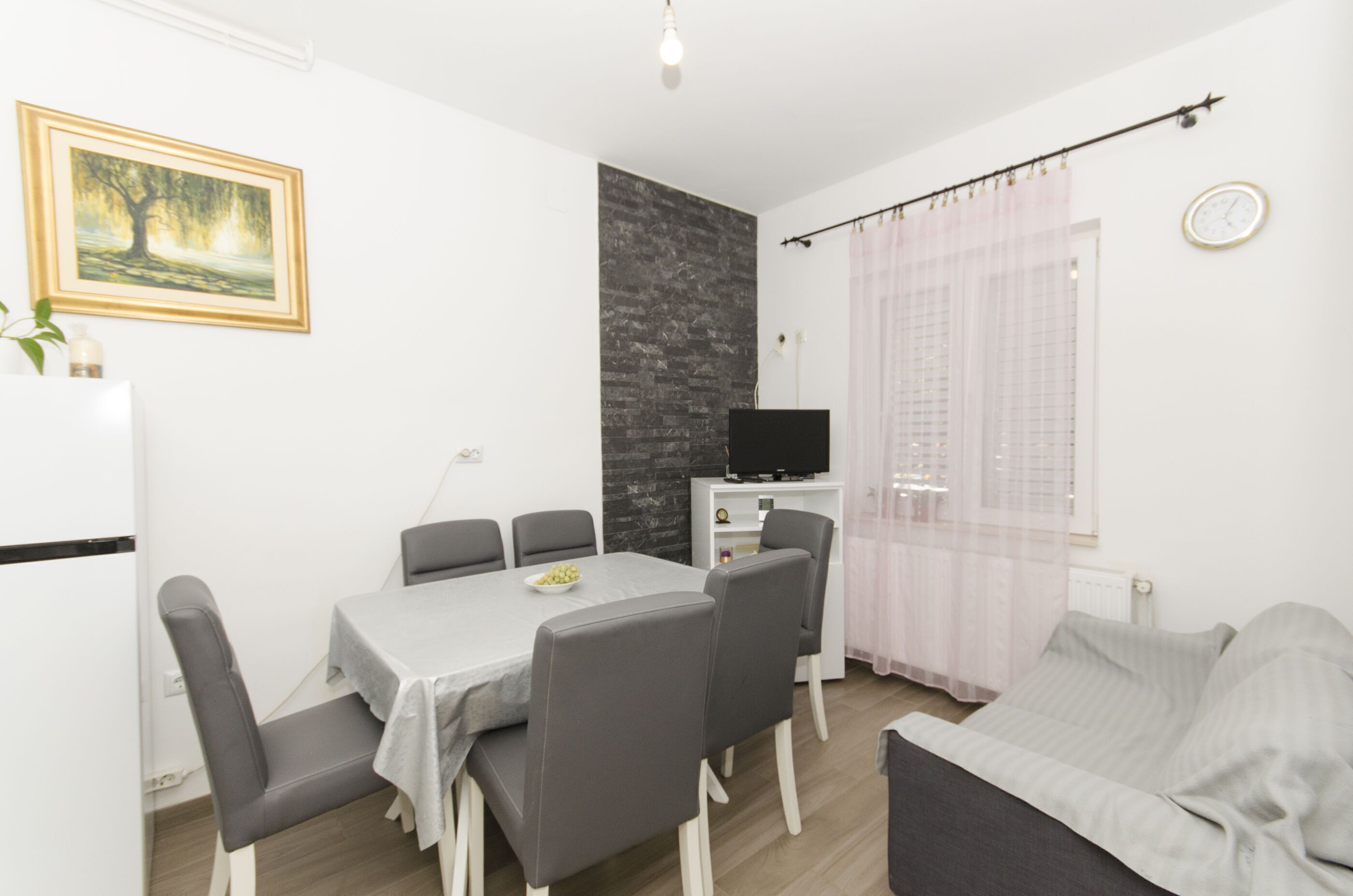 A modern living room with a dining area, a flat-screen TV, a clock, and a painting on the wall.