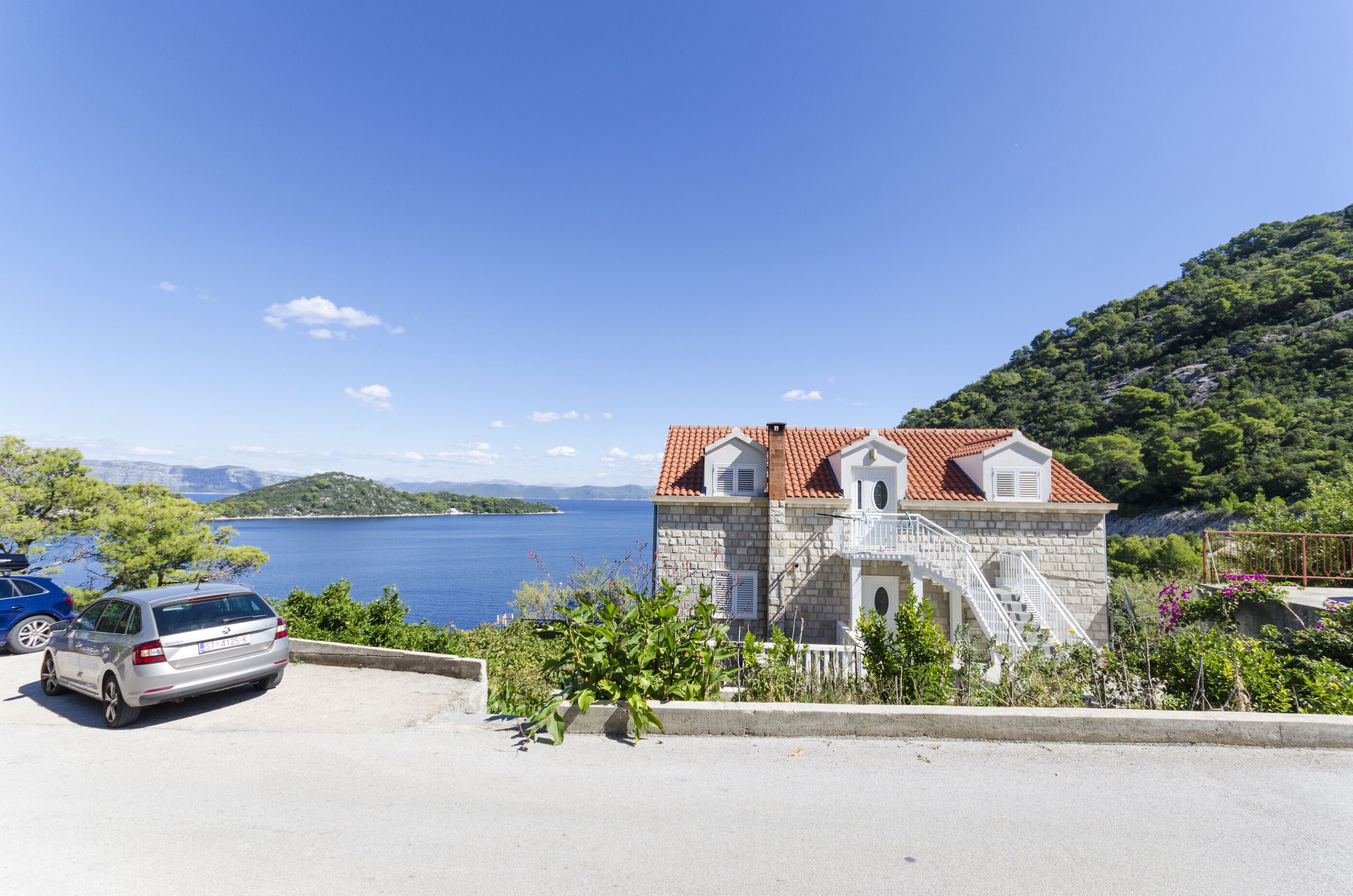 A stone building with a red-tiled roof, a staircase, and a view of a lake.