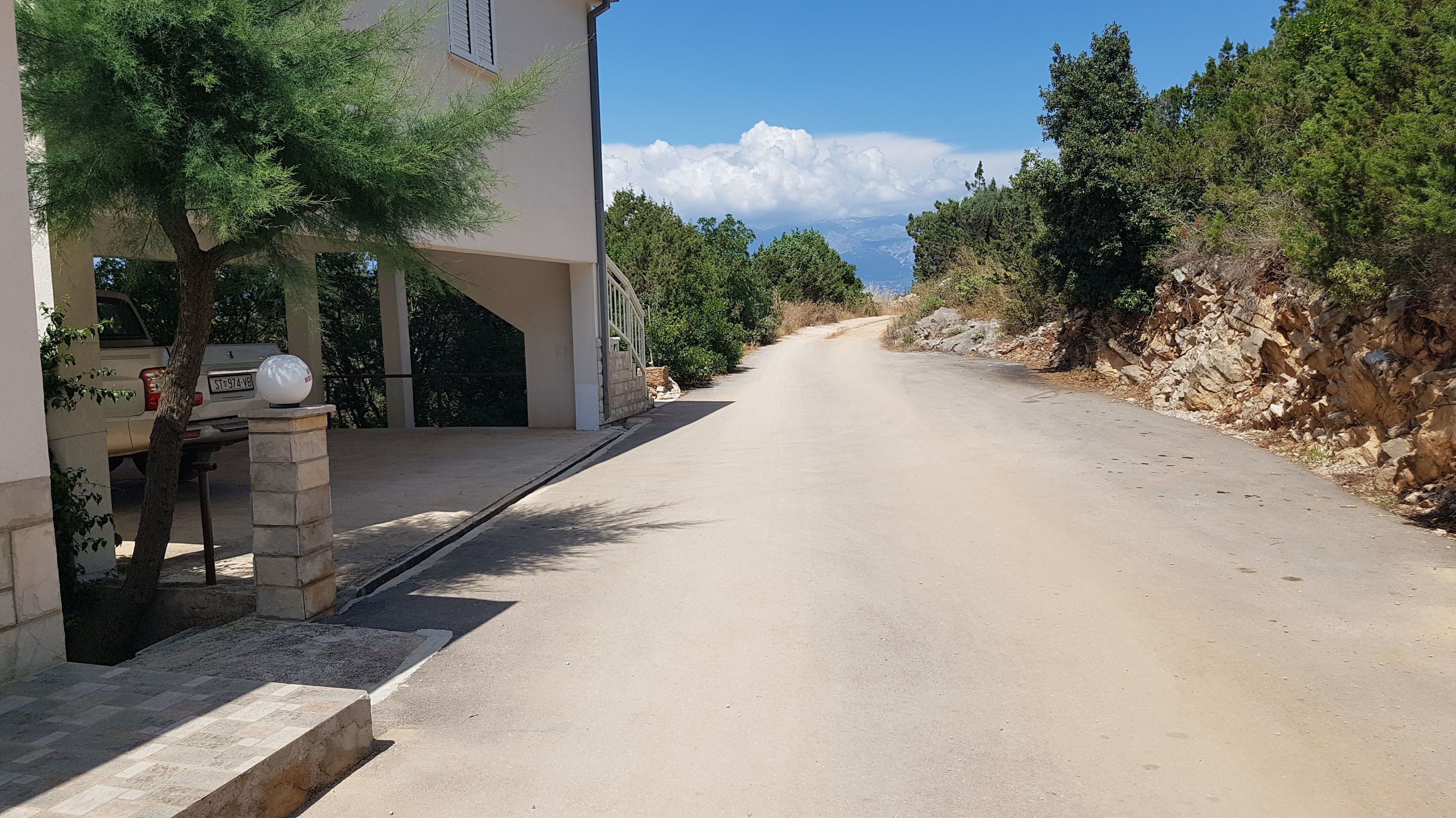 A quiet, paved road flanked by trees and a building with a stone entrance.