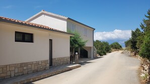 A two-story house with a tiled roof, a stone base, and a paved driveway. - Apartments Teo i Ivana (Bogomolje)
