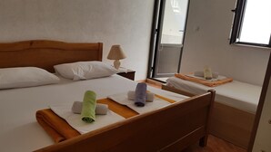 A hotel room with a wooden bed, white bedding, a nightstand with a lamp, and a window with a view. - Apartments Teo i Ivana (Bogomolje)