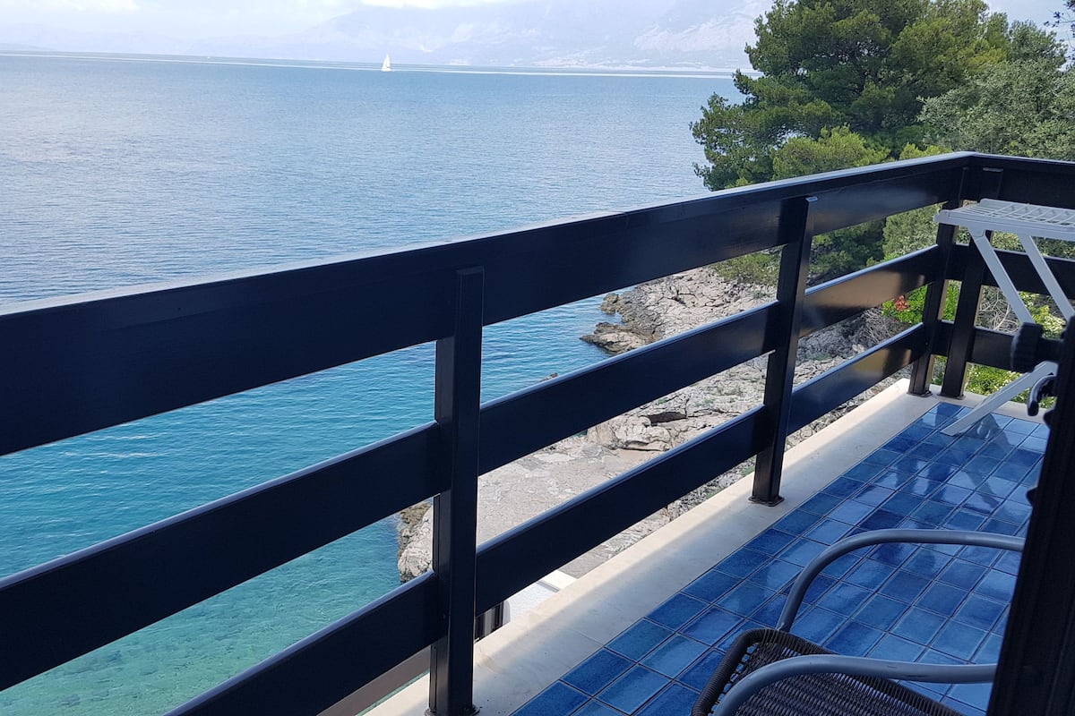 A balcony with a view of the sea, a chair, and a table.