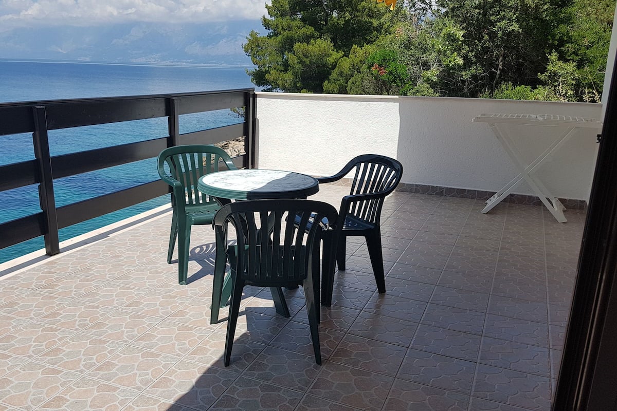 A balcony with a view of the sea, a round table, and two chairs.