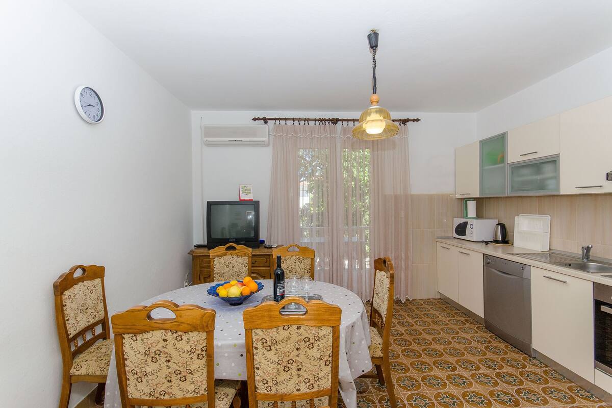 A dining area with a table, chairs, a television, and a kitchen area with cabinets and appliances.