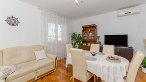 A living room with a sofa, dining table, chairs, a TV, and a wooden cabinet. - Apartments Kata (Supetar)