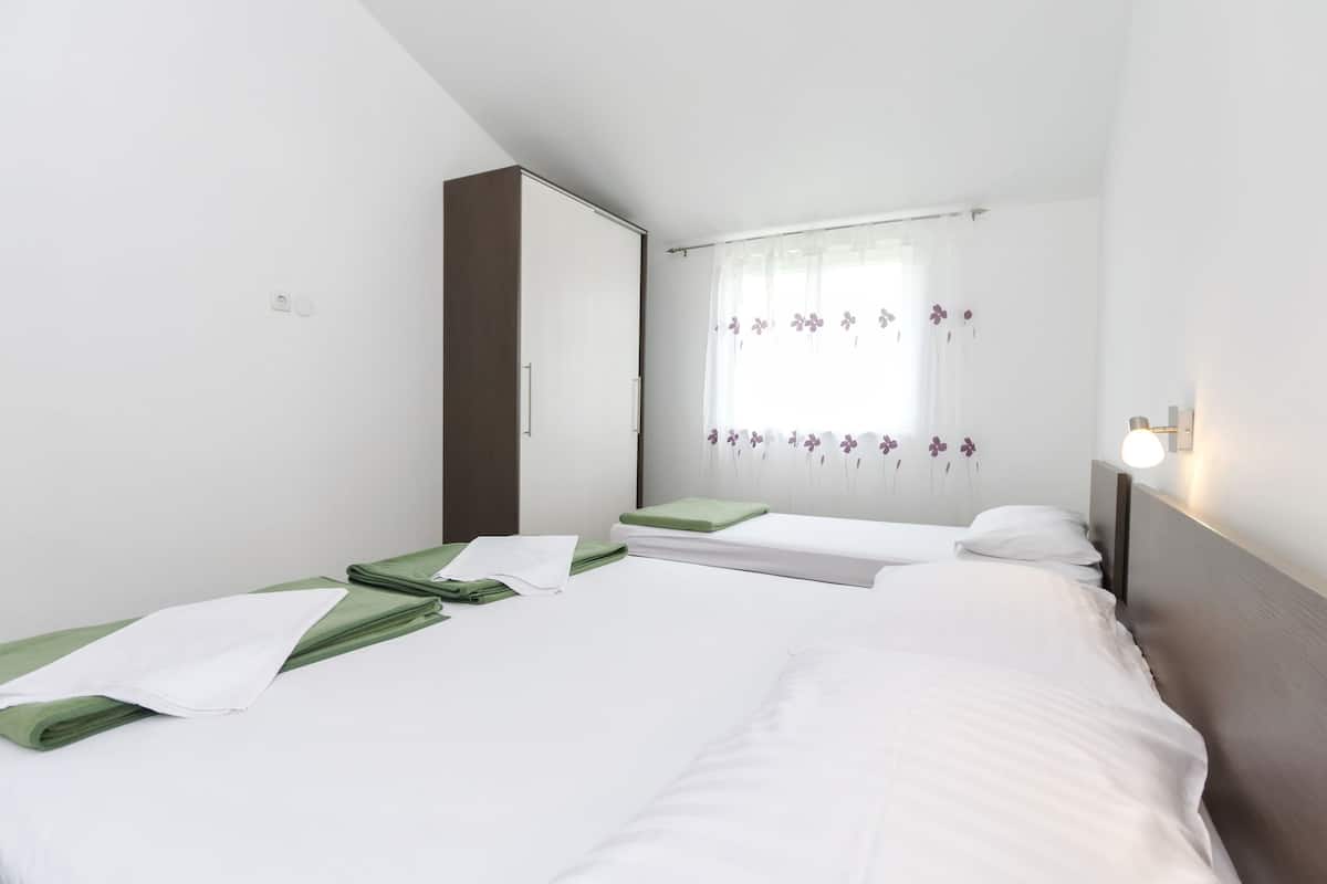 A hotel room with two beds, a wardrobe, a window with floral curtains, and a bedside lamp.