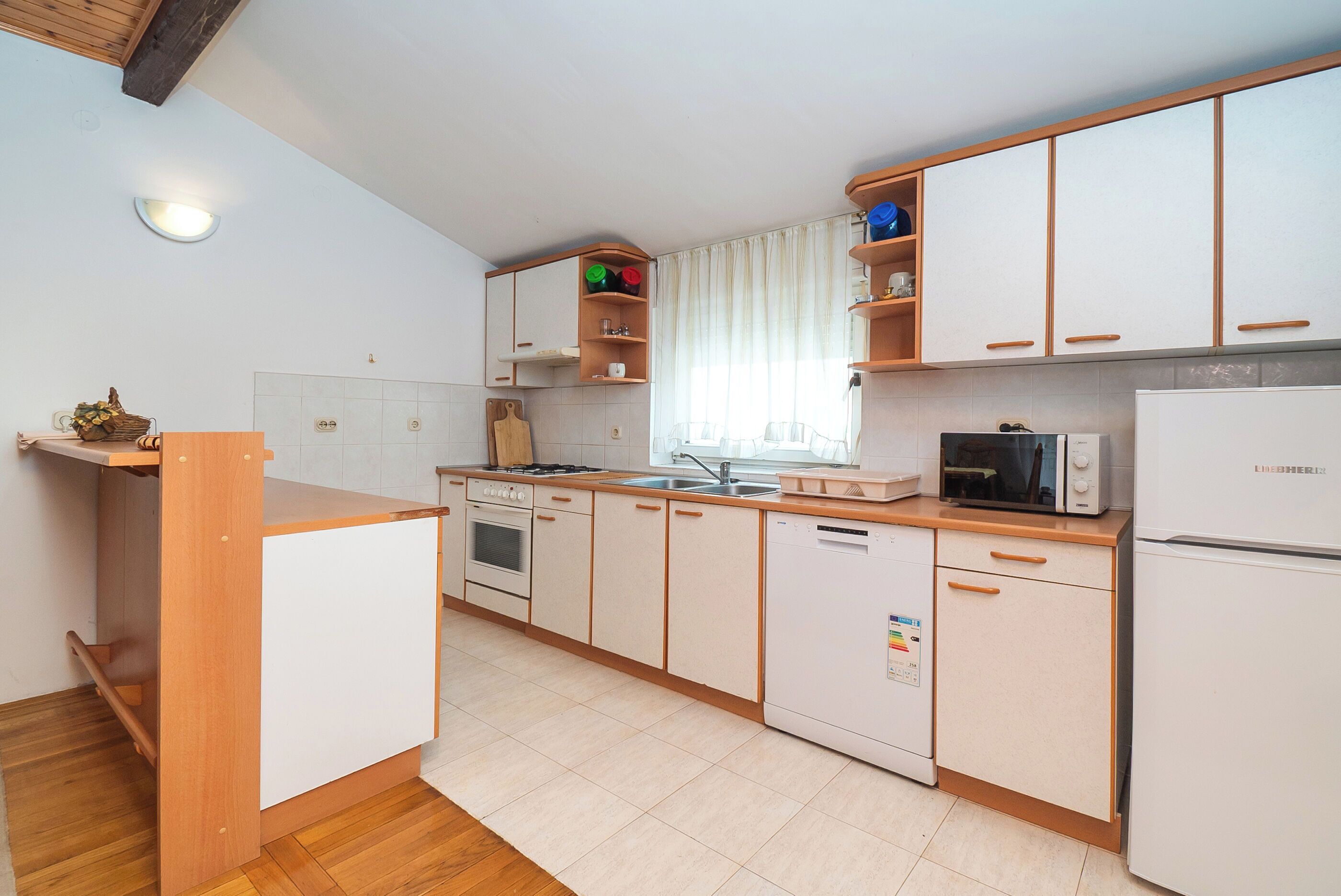 Cozinha compacta com armários de madeira, máquina de lavar louça, micro-ondas e fogão.