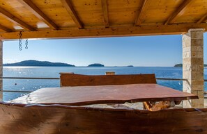 A wooden table and benches under a wooden roof overlooking a body of water with distant islands. - Apartments Ivan (Prizba)