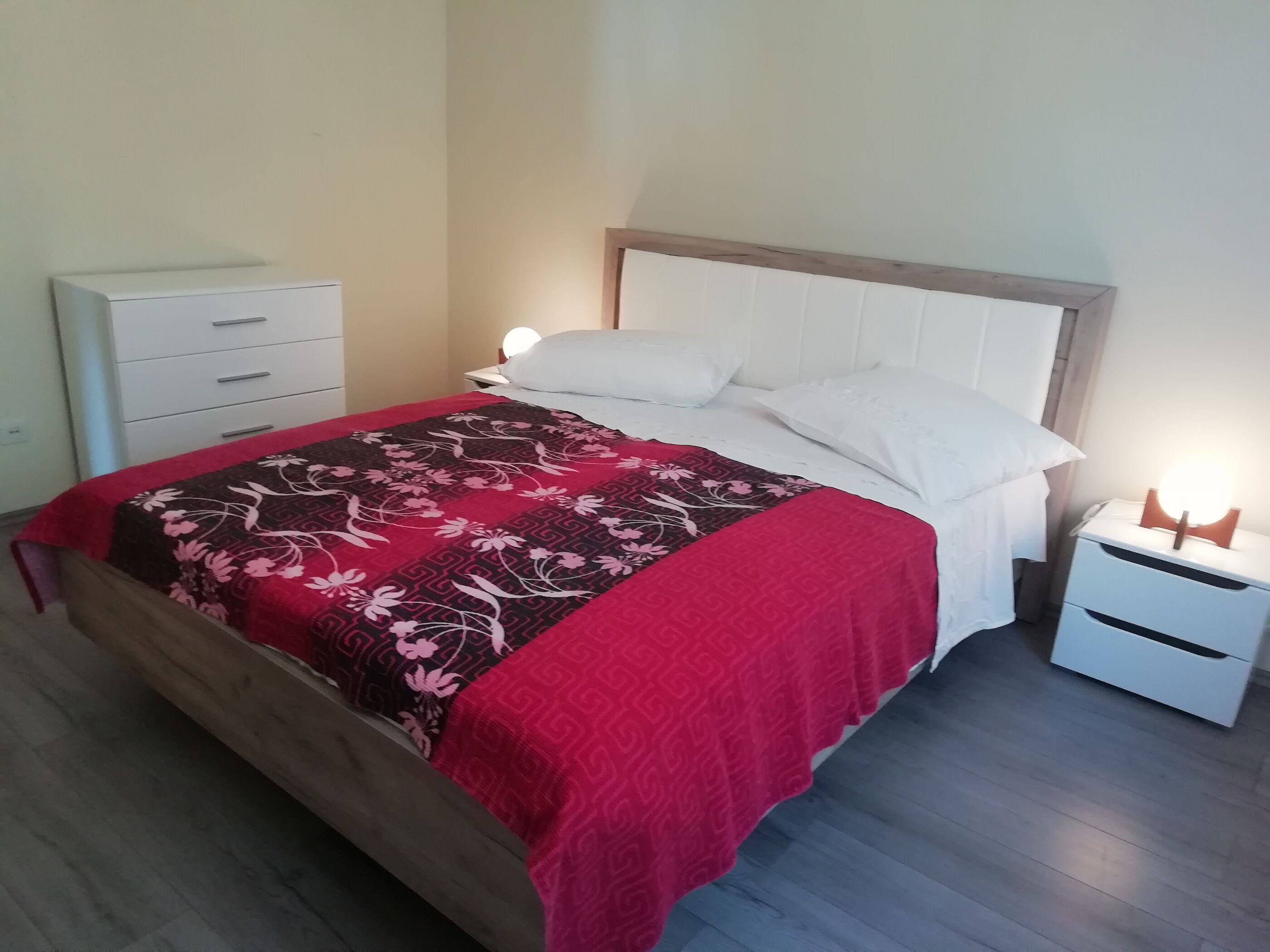 Una cama bien hecha con una colcha de estampado floral, almohadas blancas y una lámpara de noche.