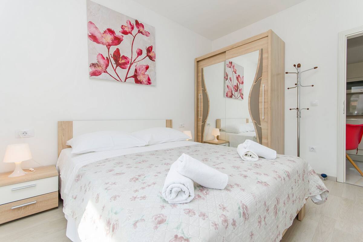 A neatly made bed with floral bedding, a bedside lamp, and a large mirror.