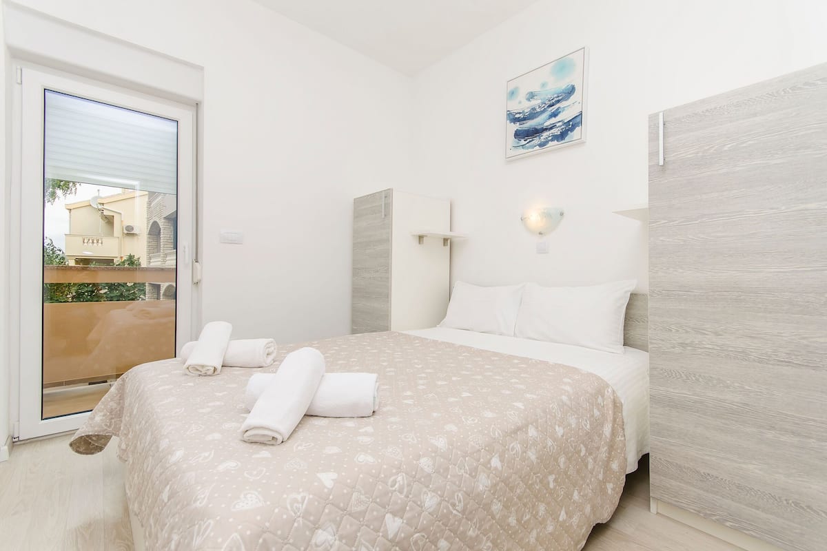 A bedroom with a bed, a door to a balcony, a wall-mounted light, and a painting.