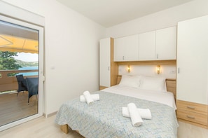 A bedroom with a bed, a wooden headboard, two bedside lamps, a balcony with a chair, and a view of the sea. - Apartments A-Z (Stara Novalja)