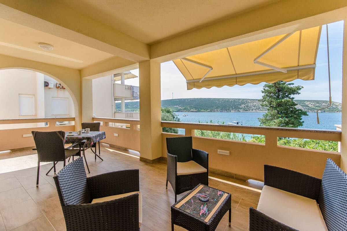 A balcony with wicker furniture, a table, and a view of the sea.