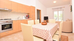 Une cuisine moderne avec des meubles en bois, une table à manger avec des chaises, un téléviseur et un balcon avec un canapé.