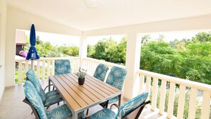 Une terrasse couverte avec une table en bois et des chaises à motifs floraux bleus, donnant sur un paysage verdoyant et luxuriant.