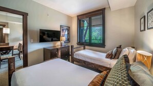 Une chambre d’hôtel avec deux lits, une télévision, un bureau et une fenêtre donnant sur un espace verdoyant.