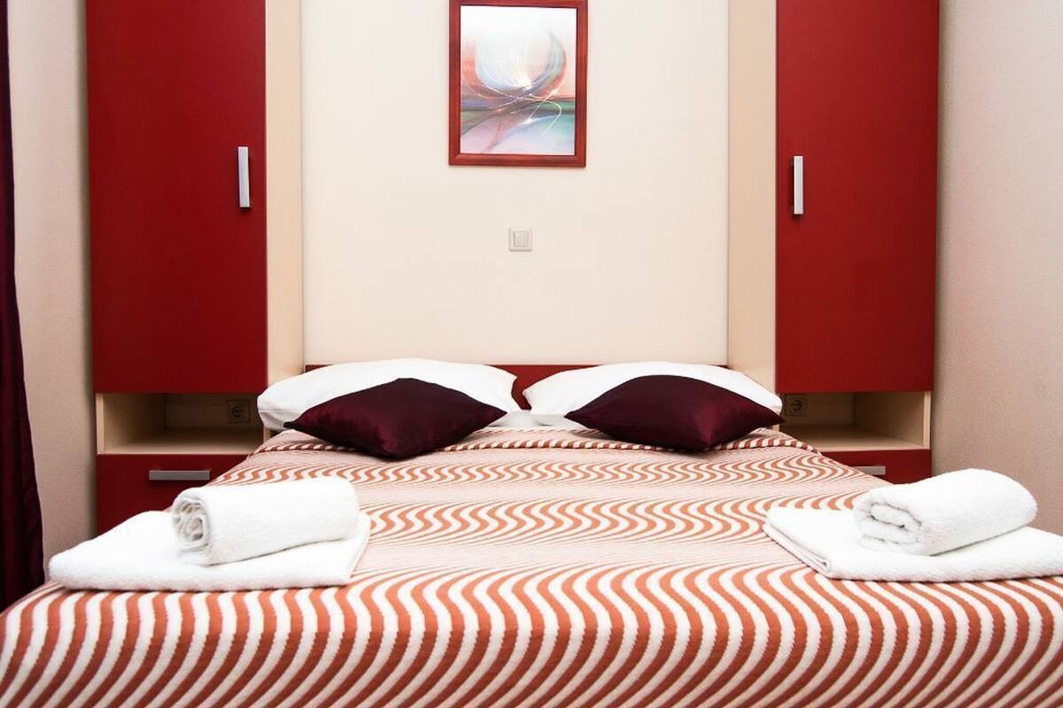 A hotel room with a bed, two pillows, a red wall, and a painting.