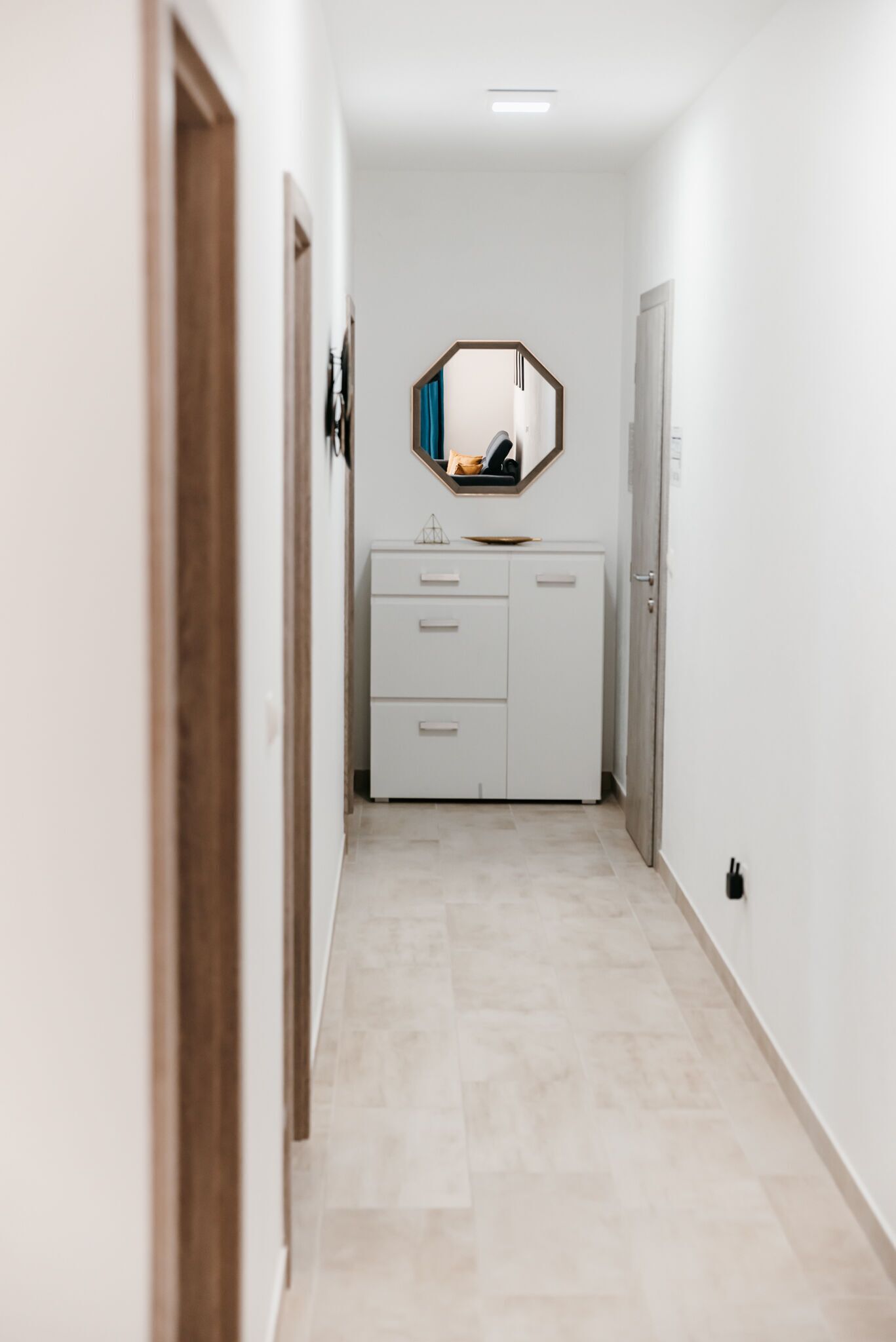 A narrow hallway with a white cabinet and a mirror on the wall.