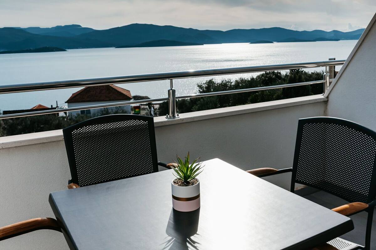 A balcony with a table and chairs overlooking a body of water and distant mountains.