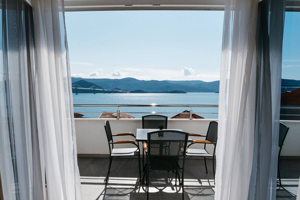 A balcony with a table and chairs overlooking a body of water and mountains.