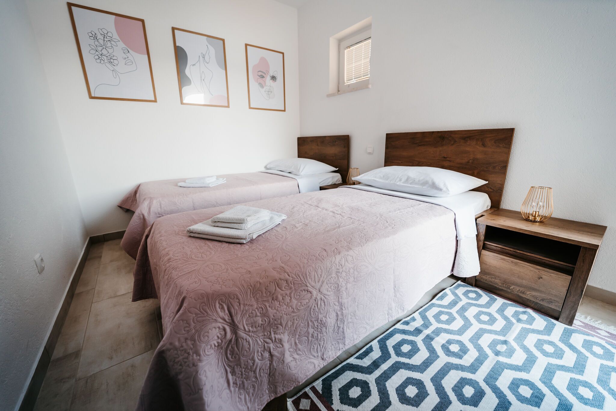 A bedroom with two beds, a wooden nightstand, and a patterned rug.