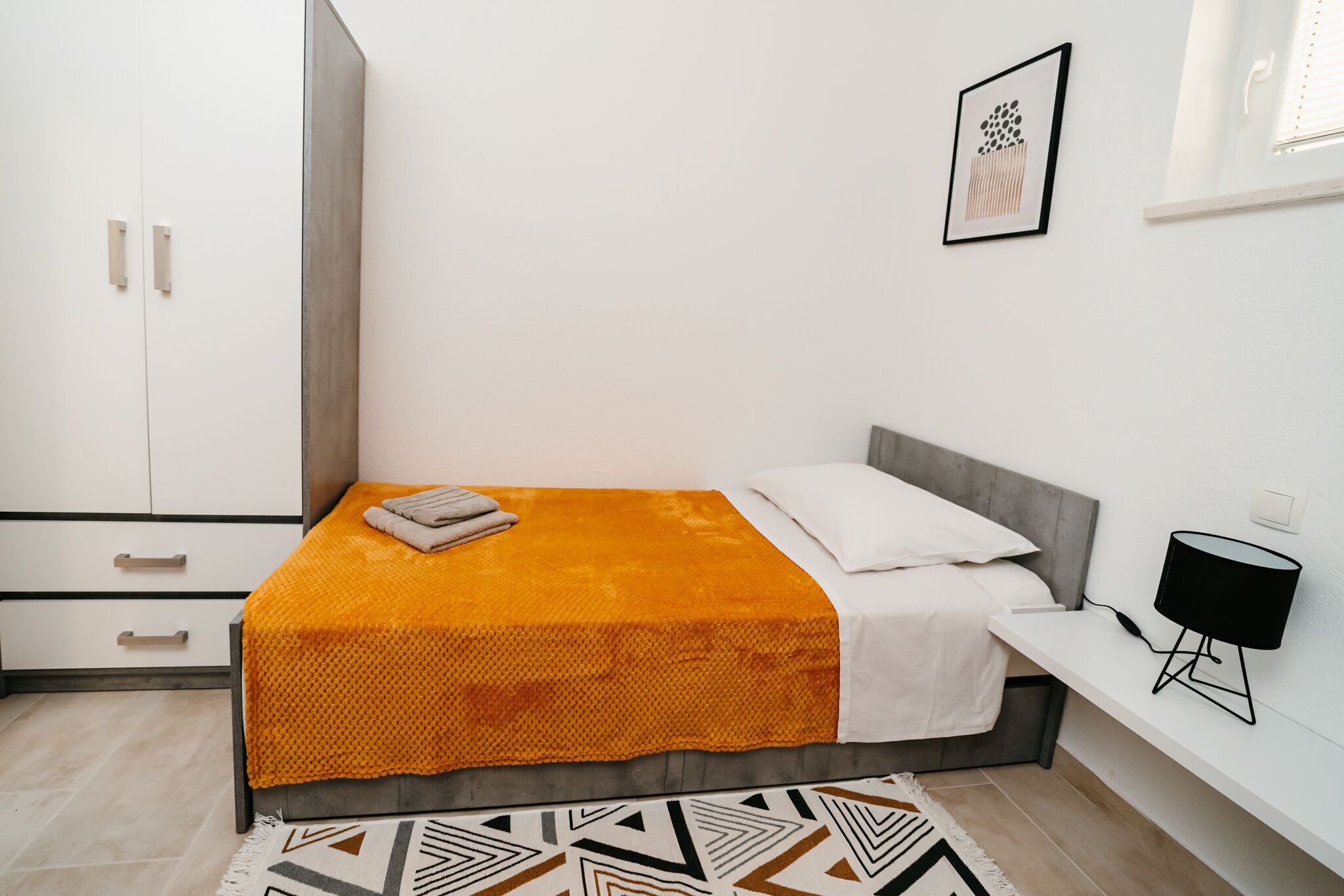 A bedroom with a bed, a nightstand, a lamp, and a wardrobe.