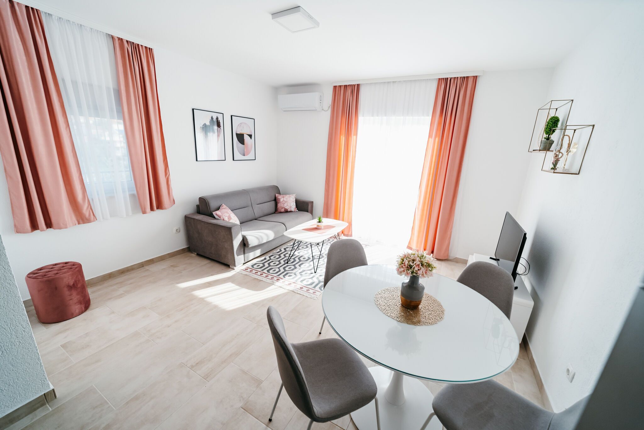 Una sala de estar moderna con un sofá, una mesa redonda de vidrio y sillas, y un televisor sobre un mueble.