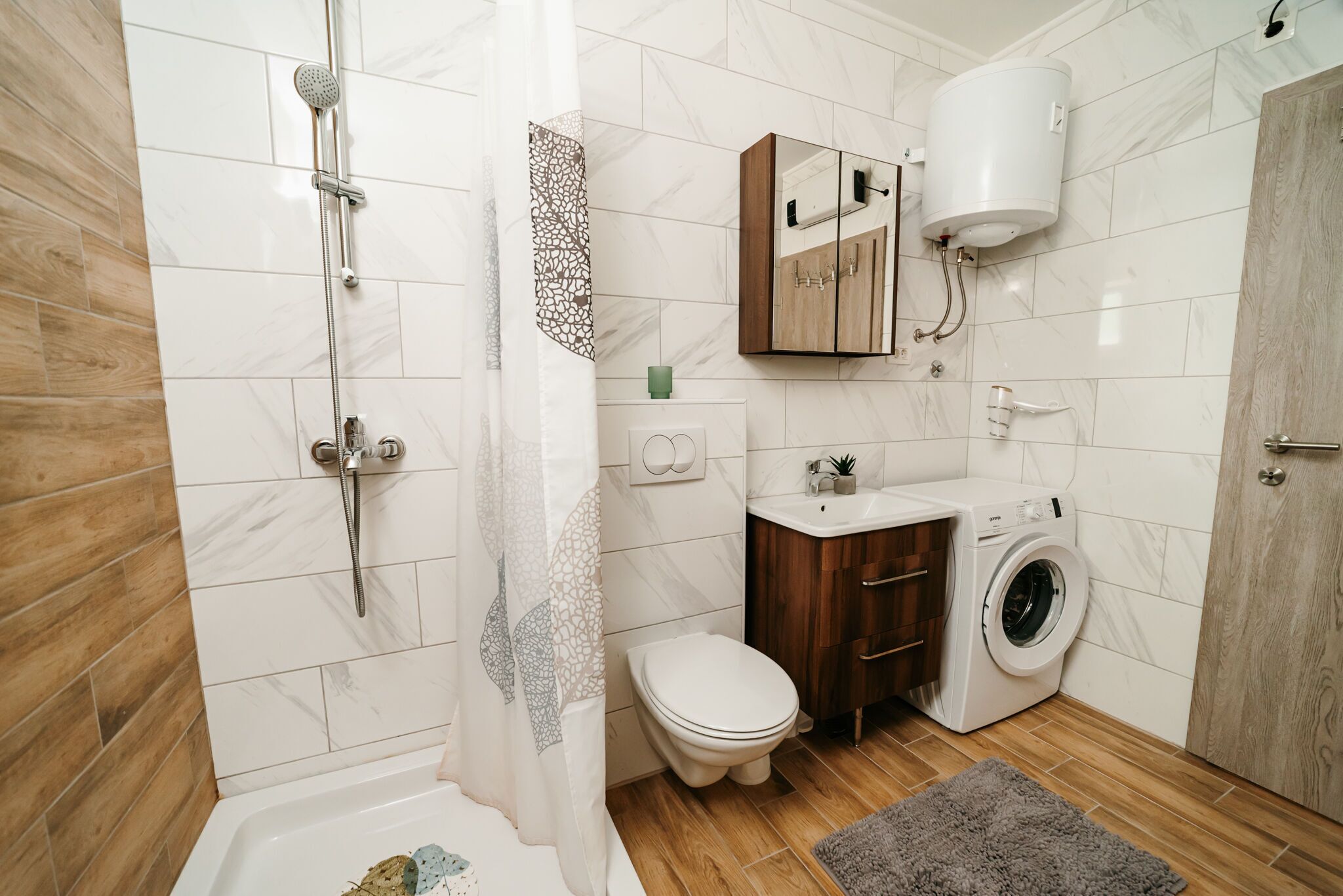A modern bathroom with a shower, toilet, sink, and washing machine.