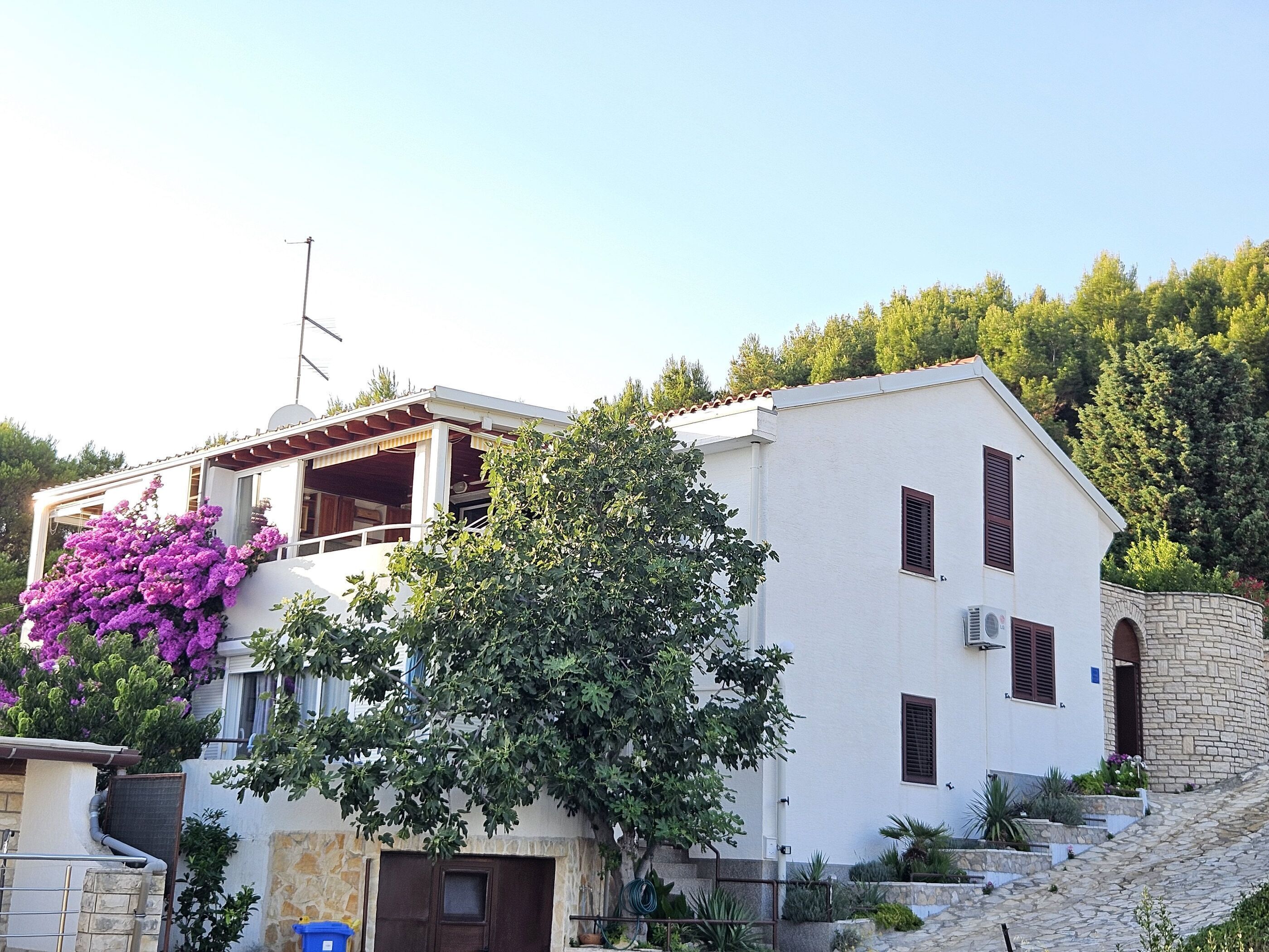 A two-story building with a balcony, a stone wall, and a garden area.