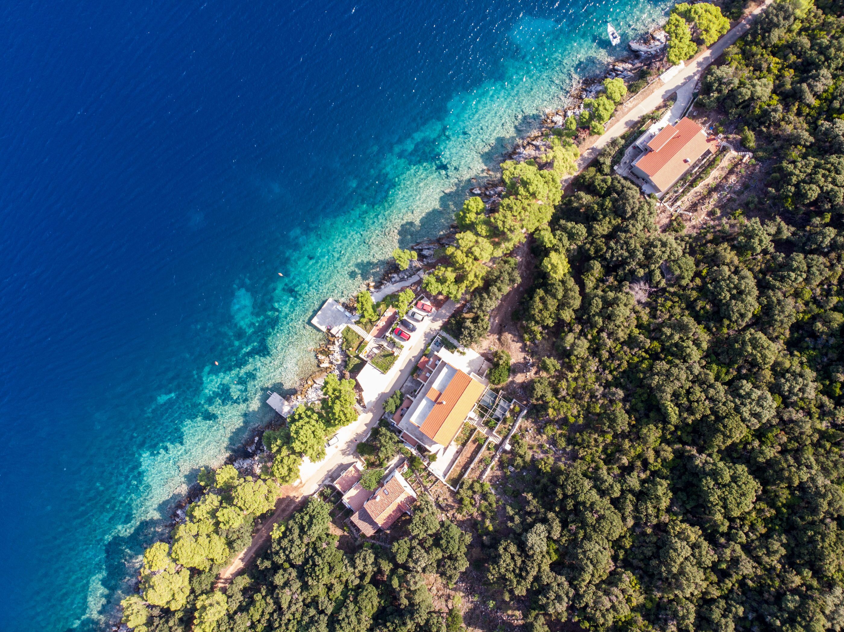 Vista aérea de una propiedad costera con varias edificaciones, aguas azules cristalinas y abundante vegetación.