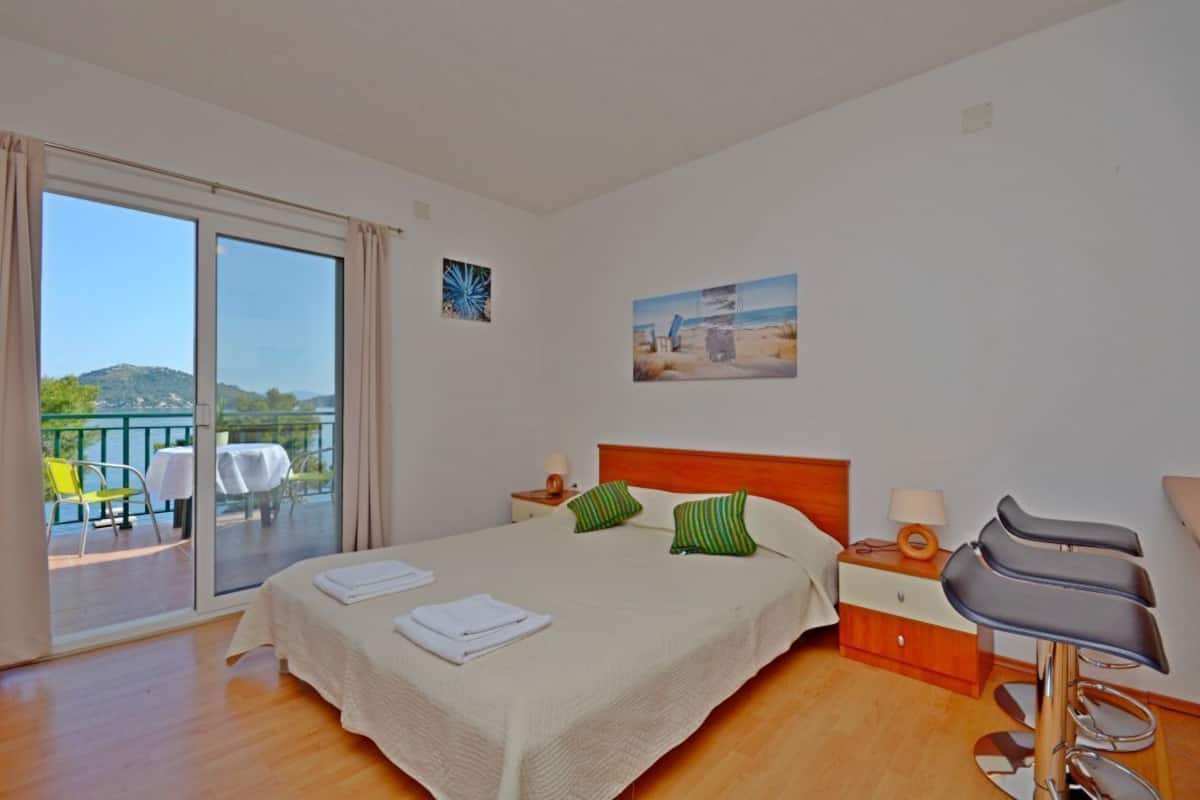 Habitación de hotel con cama, mesita de noche, silla y balcón con mesa y sillas.