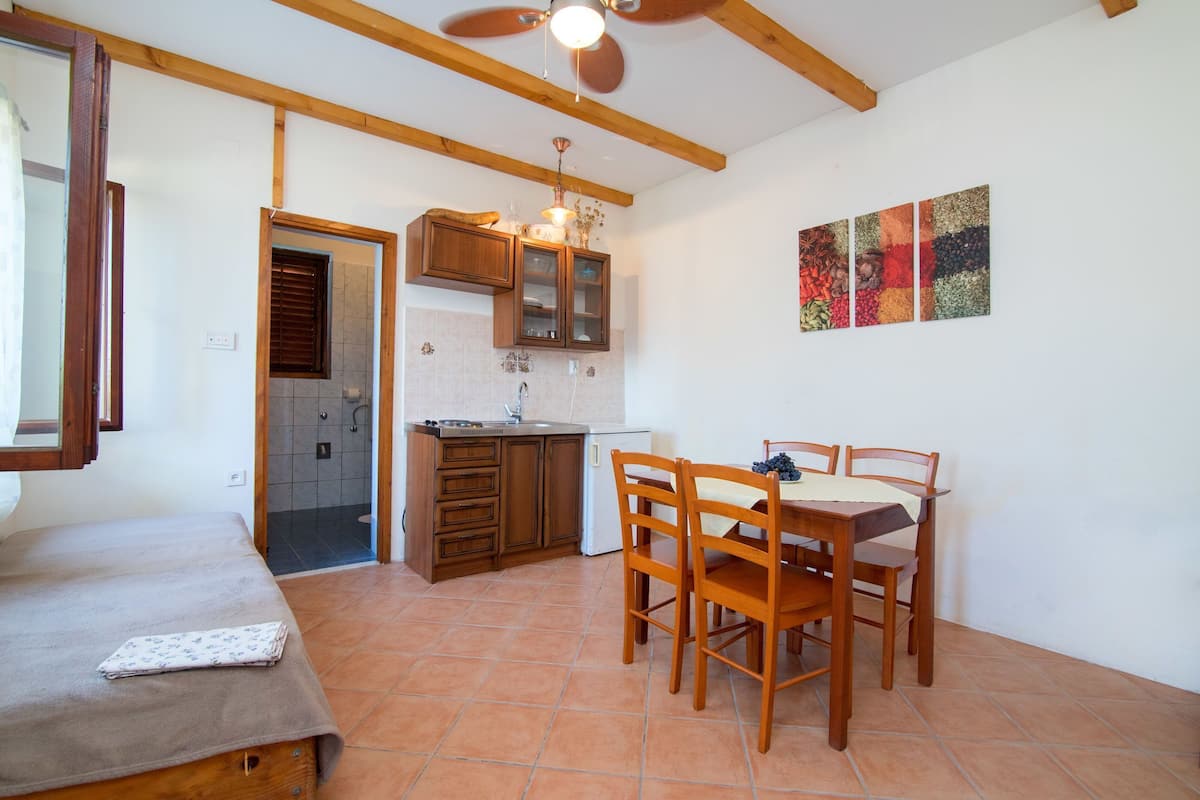 Una habitación compacta con cama, una mesa de comedor con sillas, kitchenette y ventilador de techo.