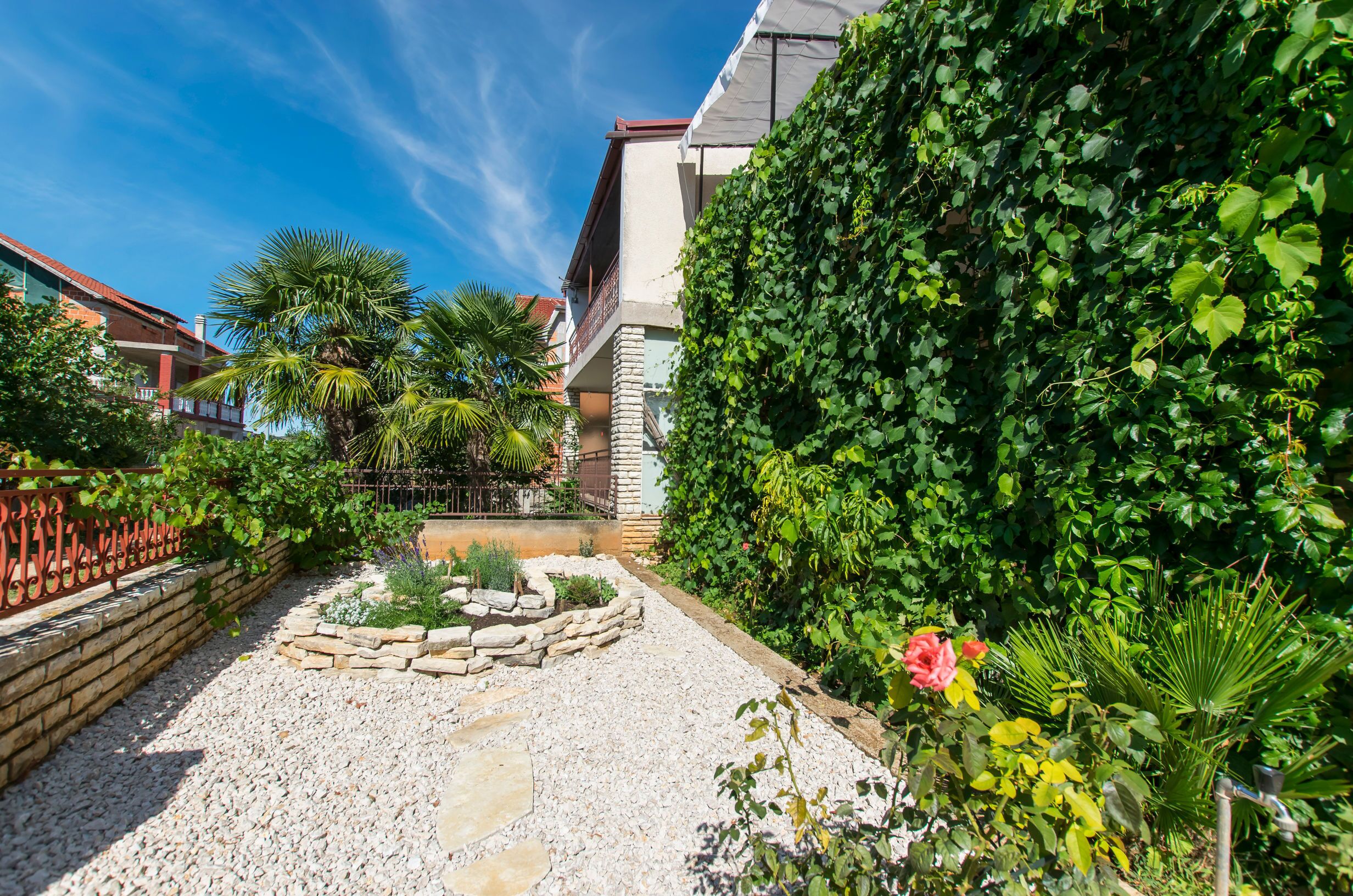 A garden with a gravel path, a stone planter, and a variety of plants.