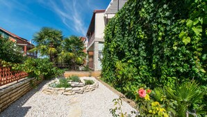 A garden with a gravel path, a stone planter, and a variety of plants. - Apartments Andrija (Pirovac)