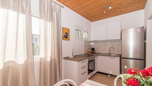 A modern kitchen with white cabinets, a stainless steel refrigerator, and a window with sheer curtains. - Apartments Andrija (Pirovac)