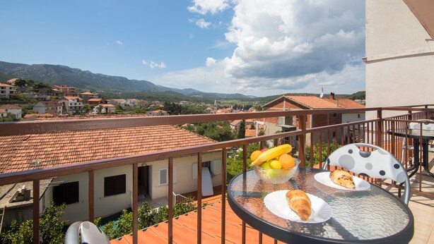 A balcony with a table set for breakfast, overlooking a town with red-roofed buildings and mountains in the distance. - Apartments Jelka (Jelsa)