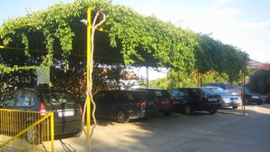 A parking area with multiple cars, a yellow fence, and a tree in the foreground. - Apartments Jelka (Jelsa)