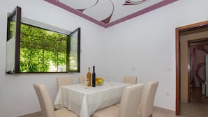 A dining area with a table set for four, a bottle of olive oil, and a bowl of fruit. - Apartments Jelka (Jelsa)
