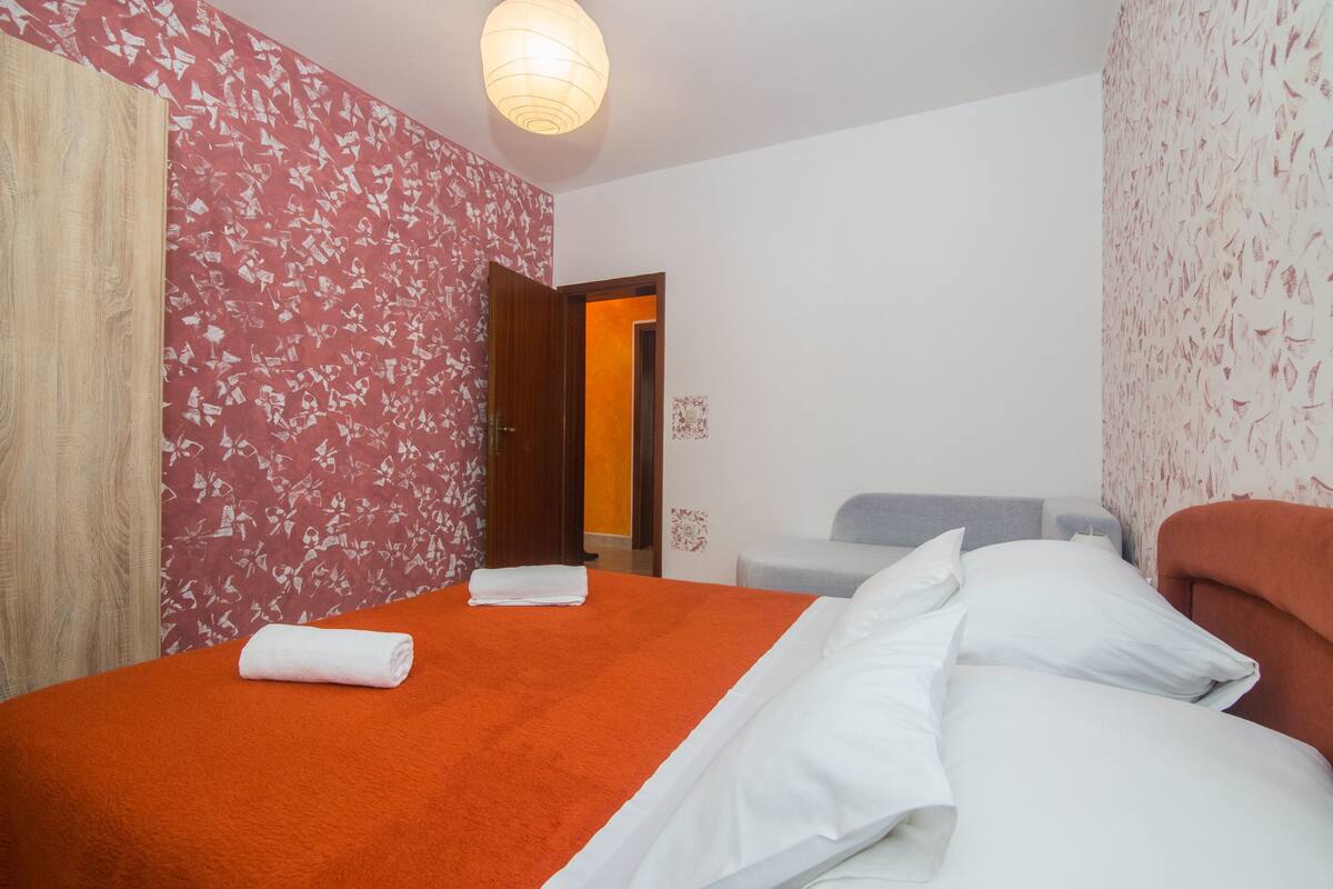 A hotel room with a bed, a chair, and a door leading to another room.