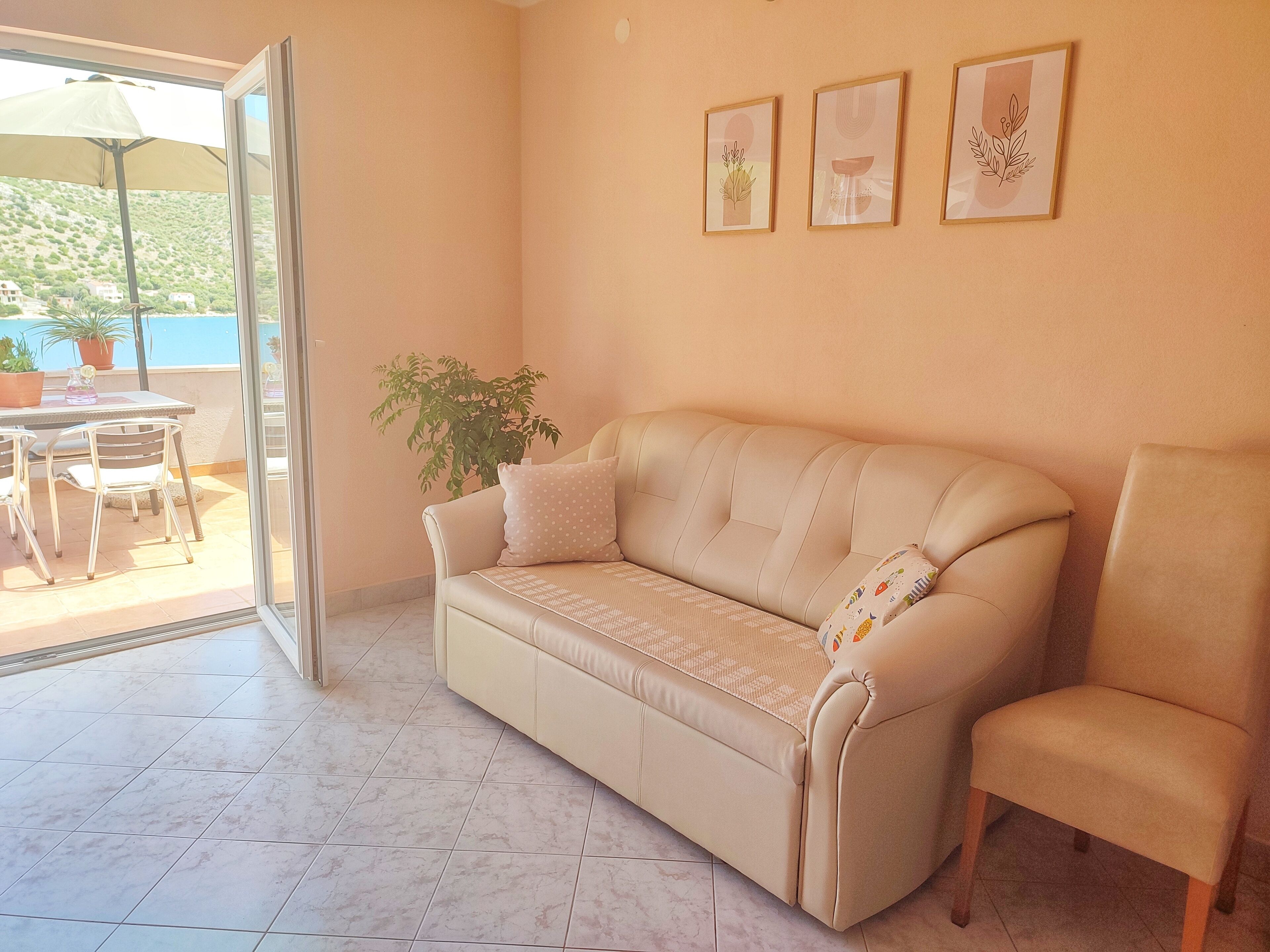 A living room with a beige sofa, a matching armchair, a dining table with chairs, and a potted plant.