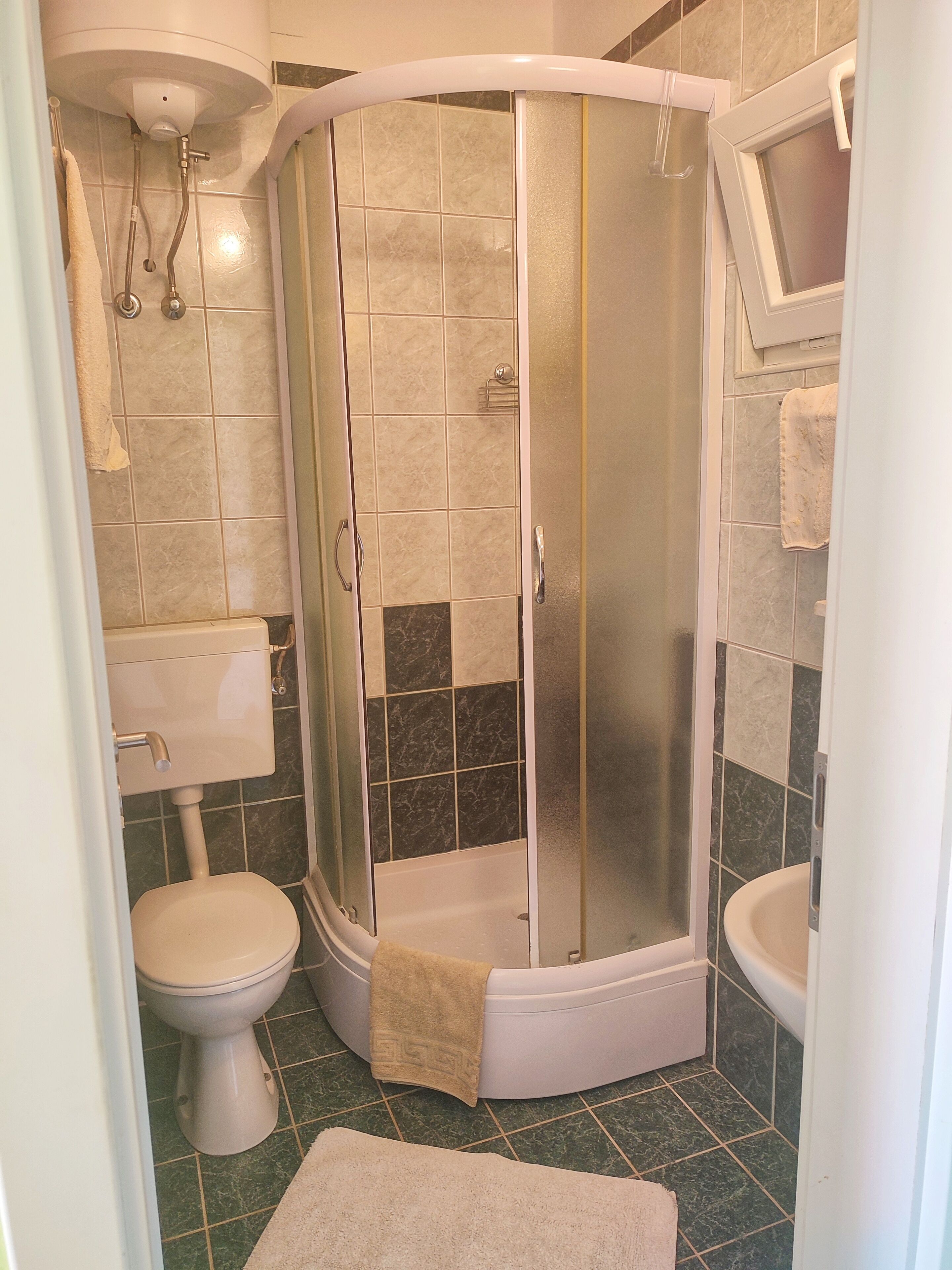 A corner bathroom with a glass-enclosed shower, a toilet, and a sink.