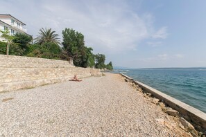 A pebbled beach with a stone wall and a building on the left. - House Iva (Jasenice)