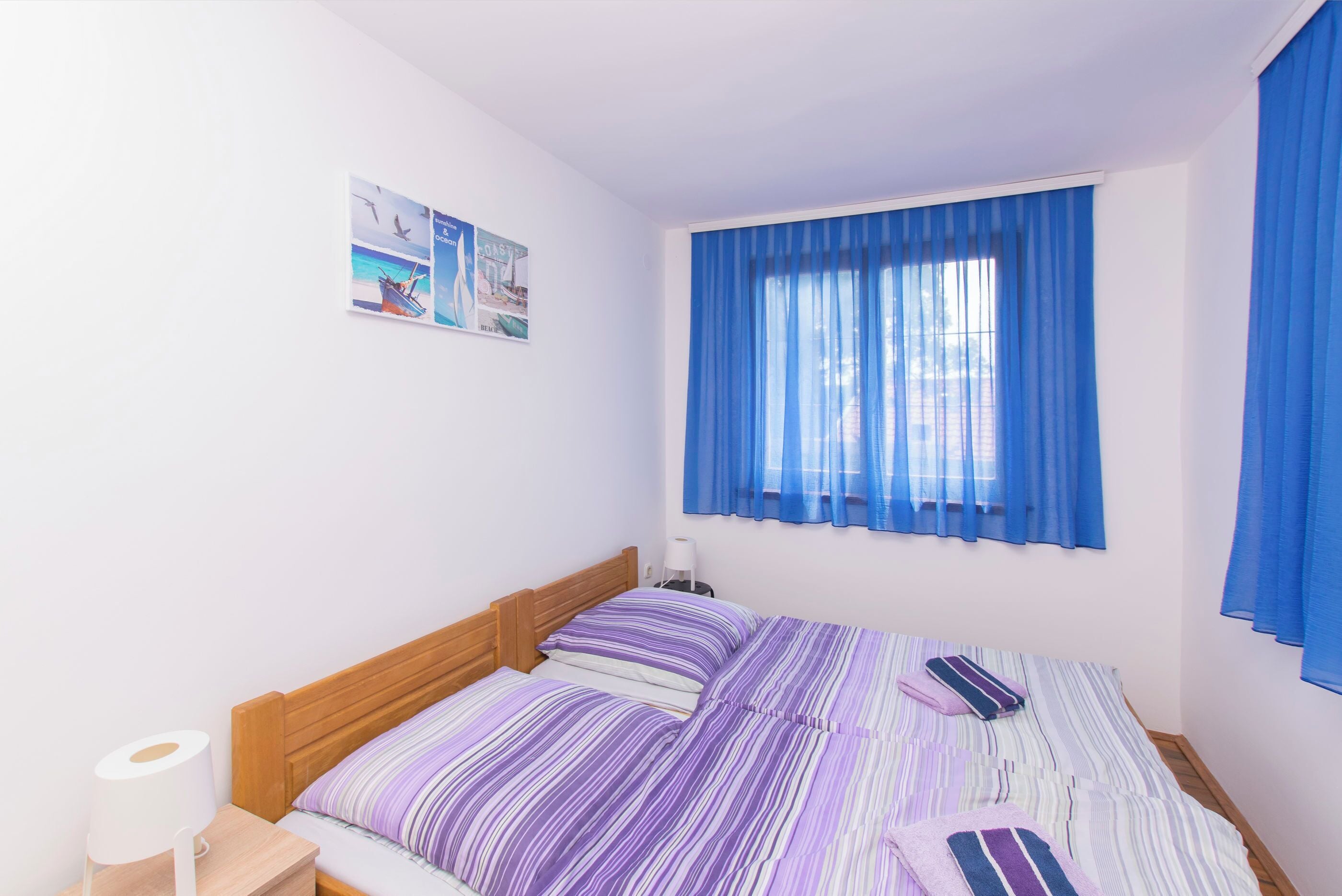 A bedroom with a bed, a nightstand, a window with blue curtains, and a wall with a poster.