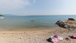 A pebbly beach with clear water, a rocky shoreline, and a distant view of mountains. - House Iva (Maslenica)