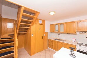 A kitchen with wooden cabinets, a stove, a sink, and a staircase leading to another level. - House Iva (Jasenice)
