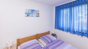 A bedroom with a wooden bed, striped bedding, a nightstand with a lamp, and a window with blue curtains. - House Iva (Maslenica)