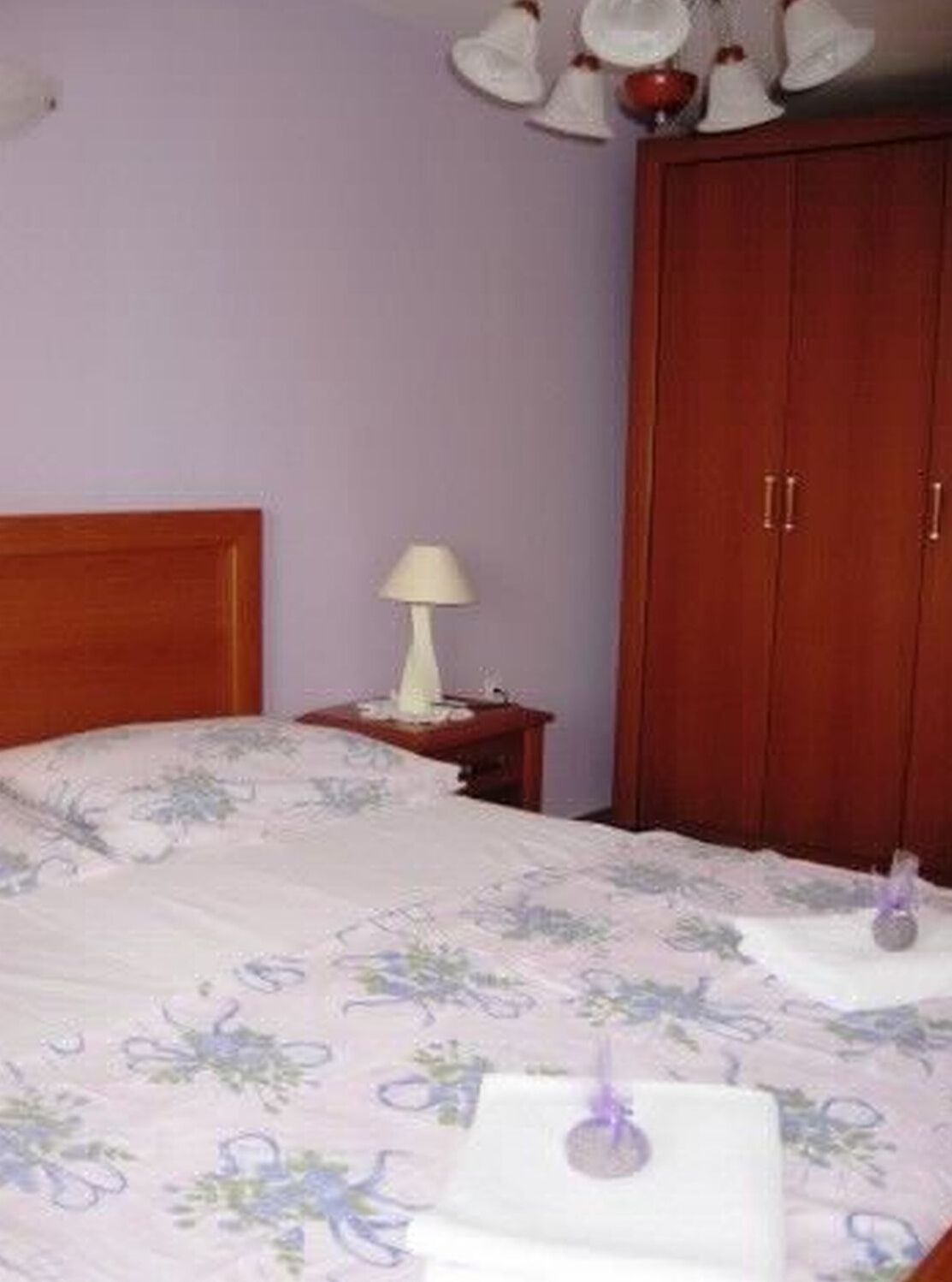 Une chambre à coucher avec une tête de lit en bois, un lit simple avec une literie à motifs floraux, une table de chevet avec une lampe et une armoire.